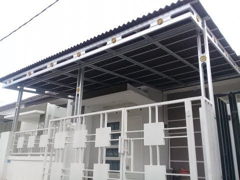 Kanopi baja ringan modern berwarna putih dengan atap gelombang hitam, terpasang rapi di depan rumah minimalis dengan pagar besi putih bergaya geometris