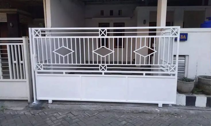 Pagar Besi Hollow Pagar besi minimalis berwarna putih dengan desain geometris berlian dan garis vertikal, dipasang di depan rumah bergaya sederhana.