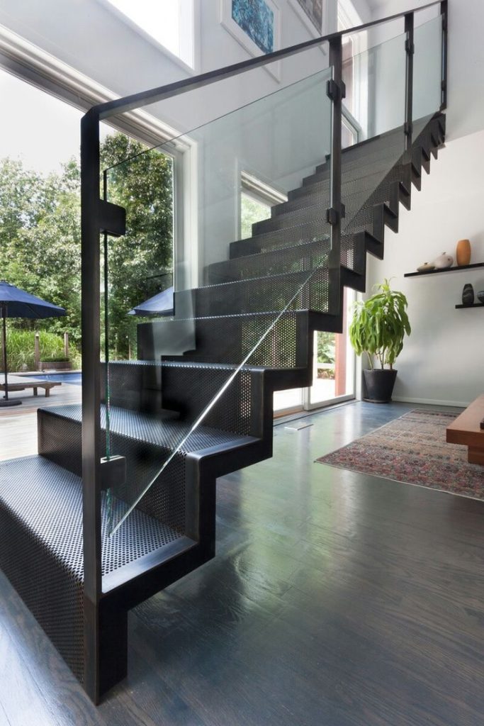 Tangga besi hitam doff dengan railing kaca.. Tangga besi hitam doff dengan desain perforated dan railing kaca transparan, menciptakan tampilan elegan dan modern pada rumah bertingkat dengan pencahayaan alami yang melimpah.