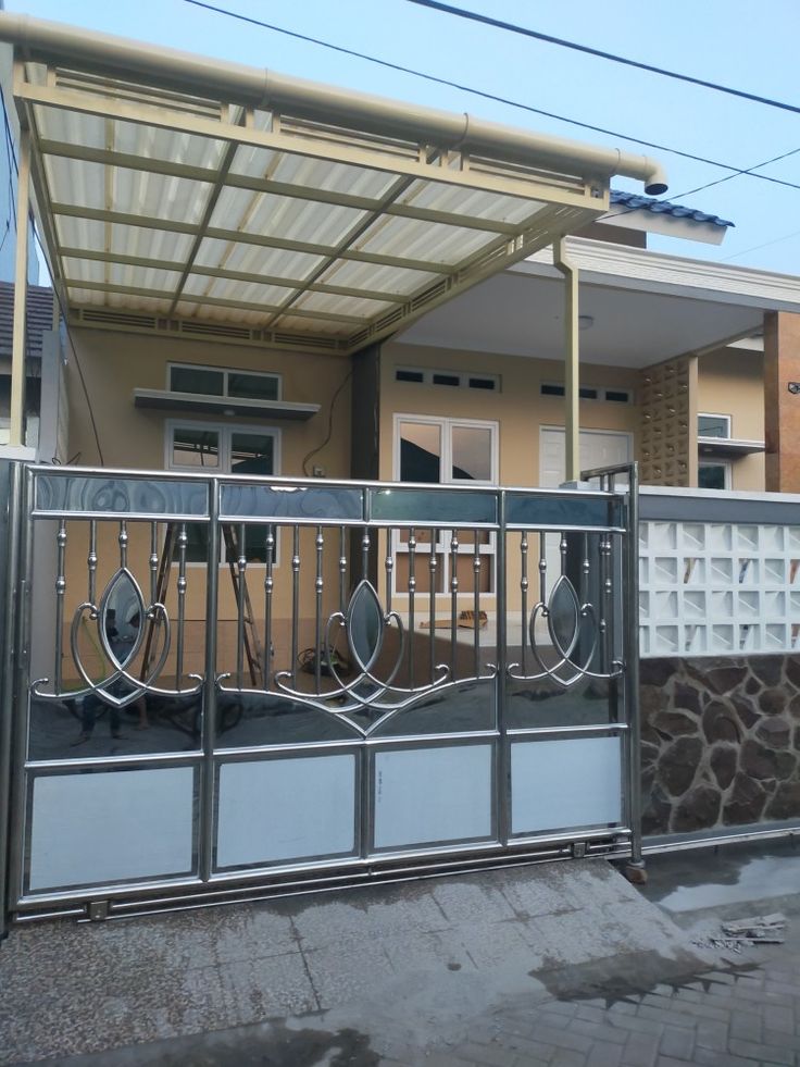 Kanopi rumah minimalis menggunakan rangka besi hollow dengan atap transparan, dipadukan pagar stainless modern di area teras depan.