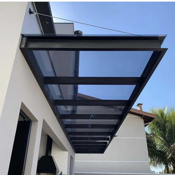 Kanopi Gantung Estetik Kanopi gantung minimalis modern dengan rangka besi hitam dan atap kaca tempered transparan, dipasang di bagian depan rumah untuk melindungi area pintu masuk tanpa menghalangi cahaya alami.