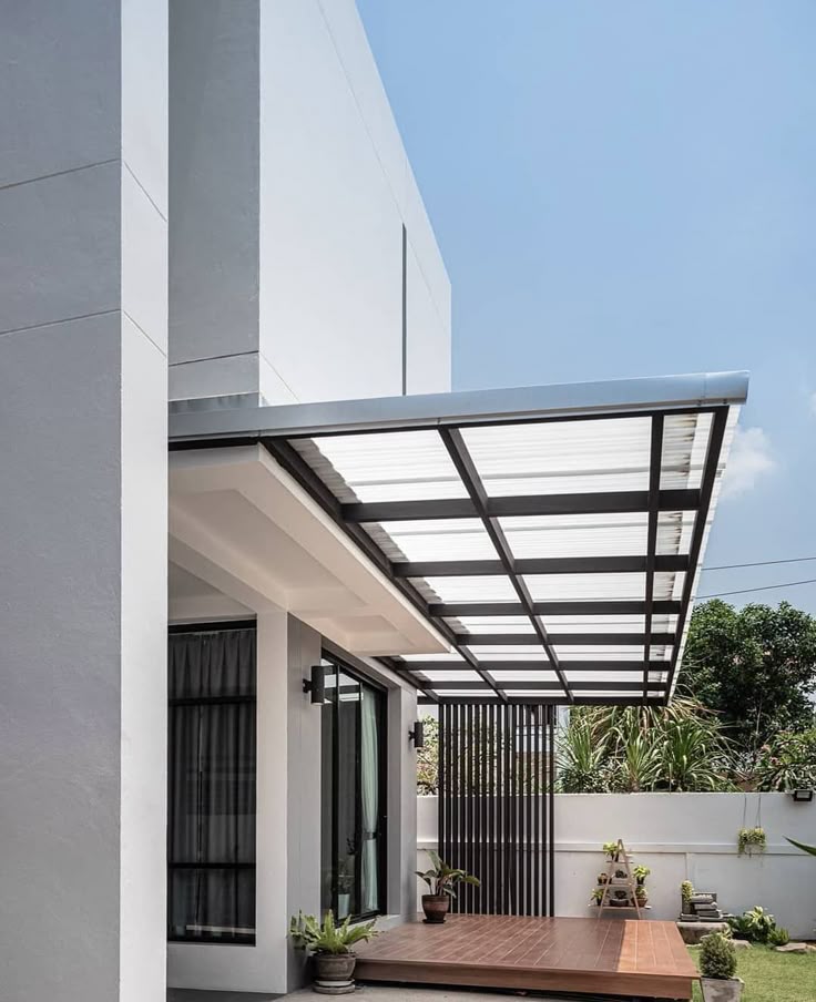 Kanopi Gantung Kanopi gantung minimalis dengan rangka besi hitam dan atap transparan di halaman samping rumah modern berwarna putih, cocok untuk lahan sempit.