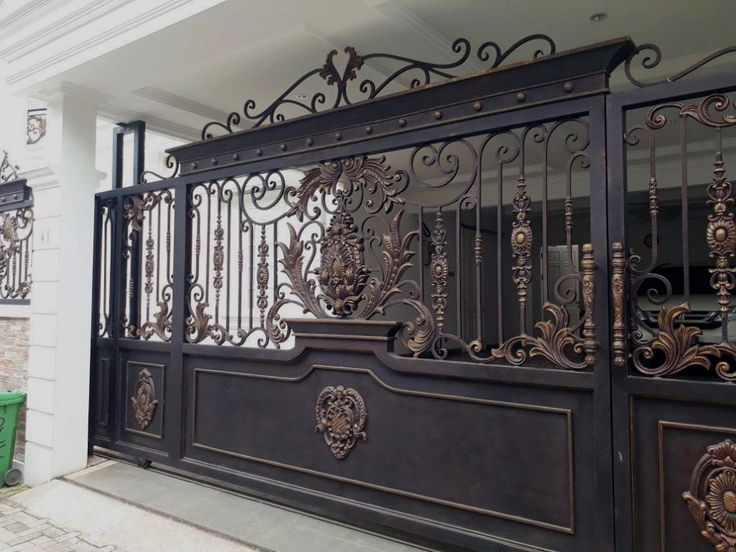 Pagar besi tempa custom bergaya klasik mewah dengan ornamen ukiran artistik warna hitam dan emas, terpasang di rumah berarsitektur elegan