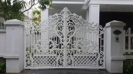 Pagar besi tempa model klasik warna putih dengan motif ukiran artistik di depan rumah minimalis elegan.